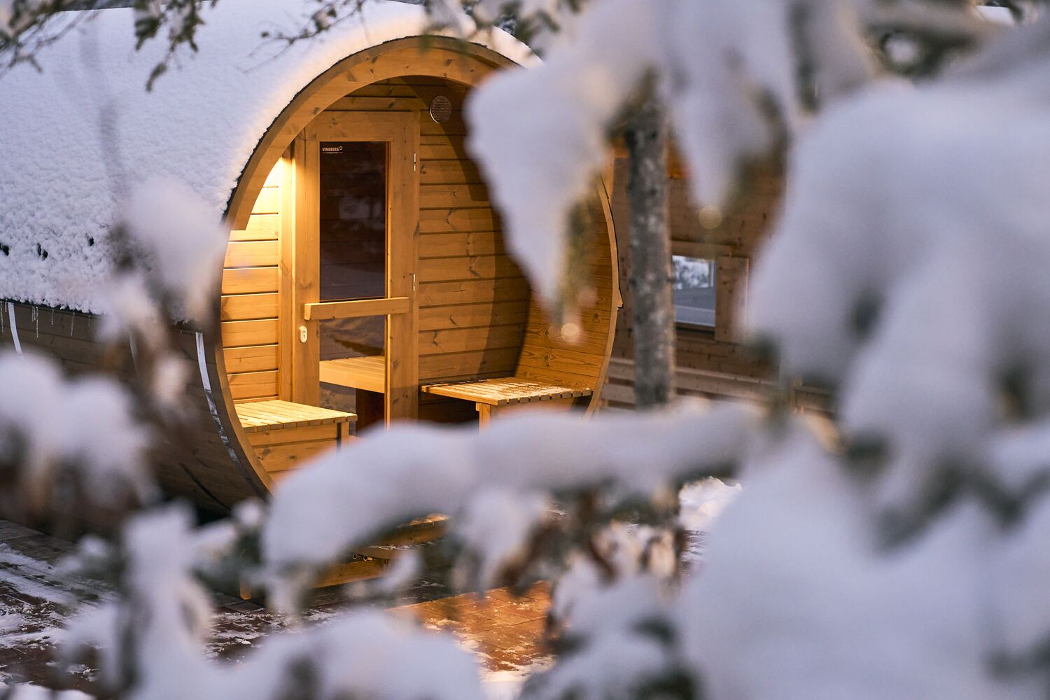Warmly lit barrel sauna in the snowy forest at dusk