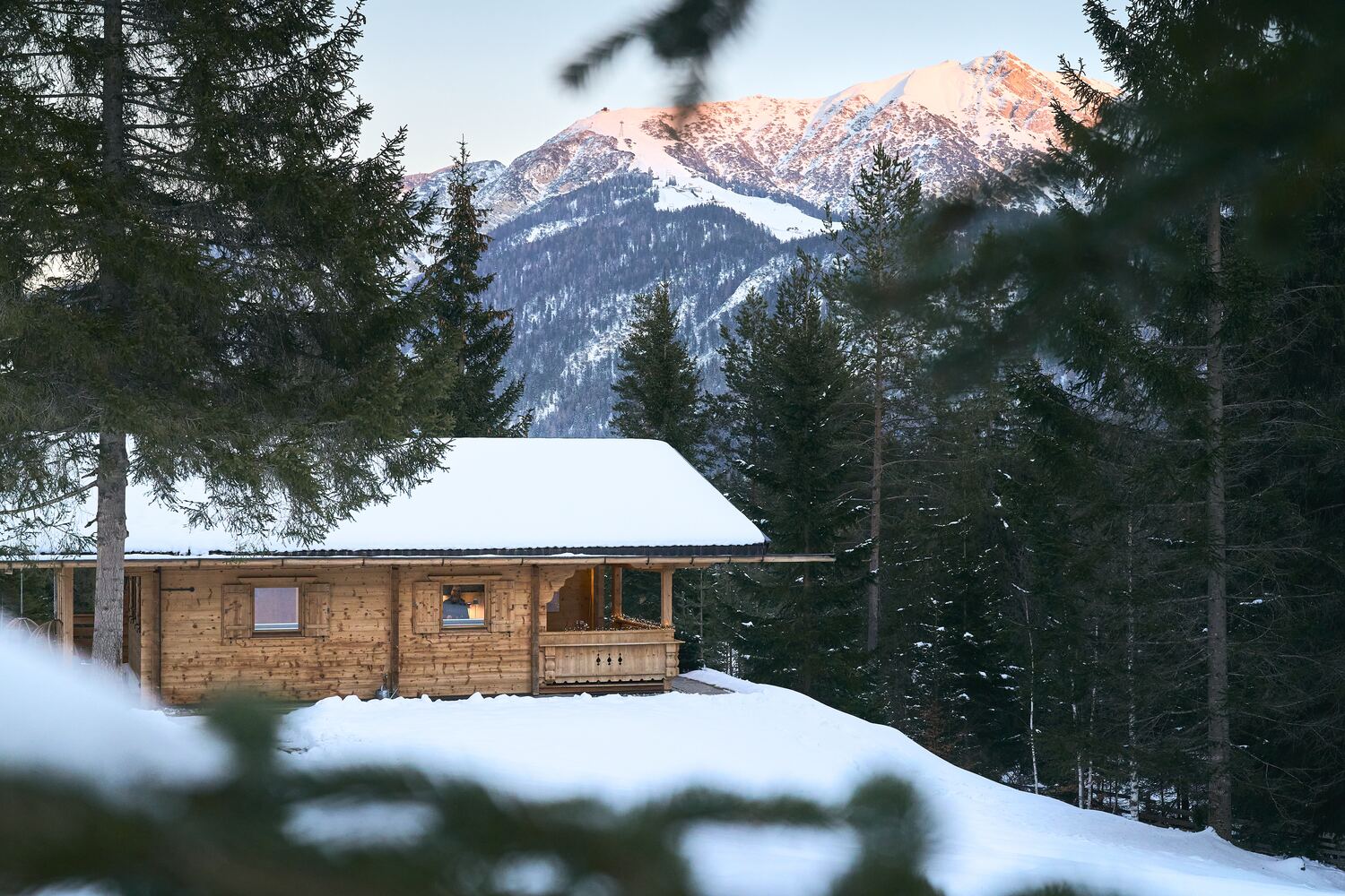 The snow-covered chalet at the forest edge, with the Seefeld mountains glowing behind it